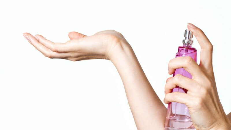 Frau sprüht Parfüm auf ihr rechtes Handgelenk