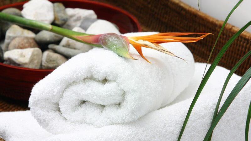 Weiße, zusammengerollte Handtücher neben brauner Schale mit Steinen