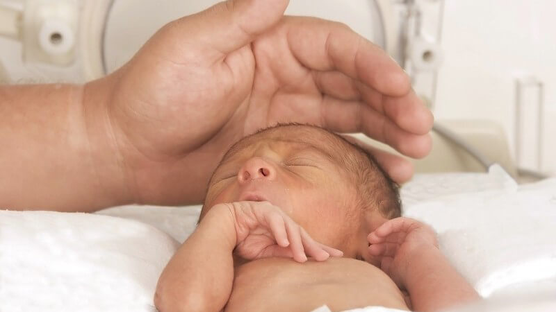 Neugeborenes in Brutkasten, Hand von Vater über seinem Kopf