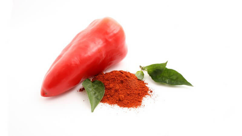 Rote Chili Schote, daneben rotes Pulver mit grünen Blättern, weißer Hintergrund