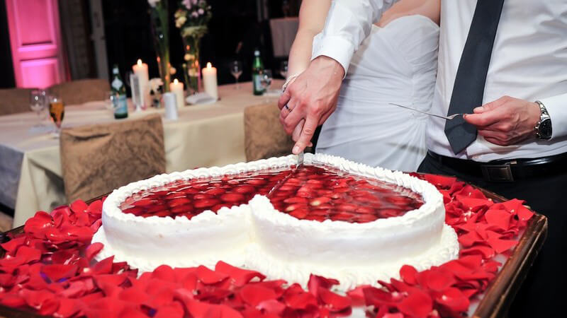 Hochzeitspaar schneidet gemeinsam eine weiße Torte in Herzform mit Erdbeeren an