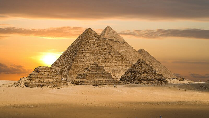 Drei Reiter in Wüste, im Hintergrund Pyramiden im Sonnenuntergang