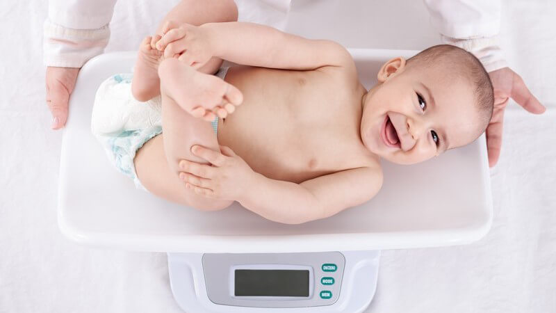 Kinderarzt wiegt ein lachendes Baby in Windel auf einer modernen Waage