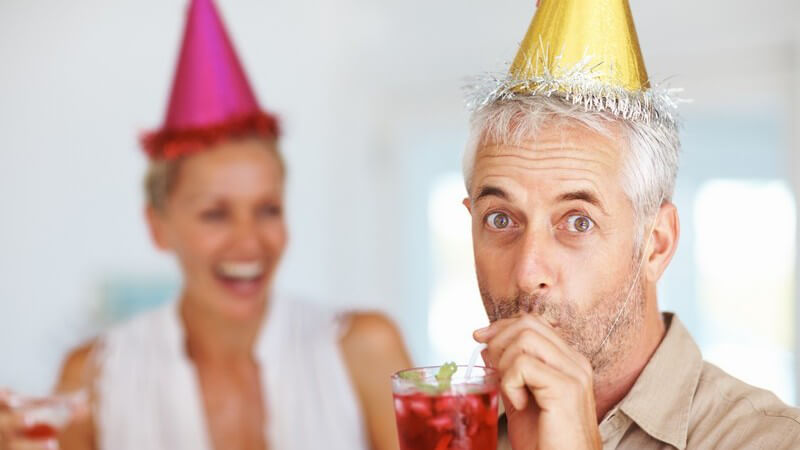 Älteres Paar mit Partyhütchen und Cocktails