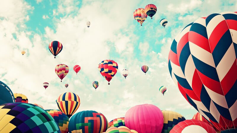 Unzählige Heißluftballons in verschiedenen Mustern und Farben steigen in den Himmel auf