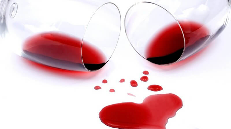 Zwei Gläser mit Rotwein gekippt, darunter Rotweinfleck in Herzform