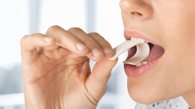 Frau steckt sich einen Kaugummistreifen in den Mund