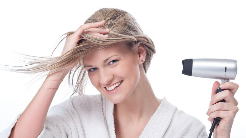 Blonde Frau im Bademantel föhnt sich die Haare mit Föhn