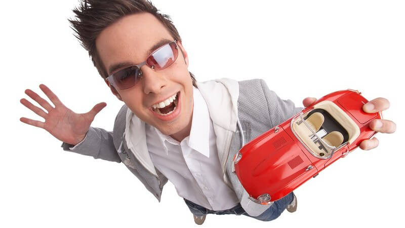 Junger, sportlicher Typ mit Sonnenbrille von oben mit rotem Modellauto