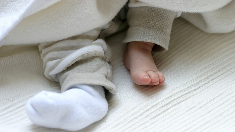 Füße eines Babys unter Decke, ein Strumpf fehlt