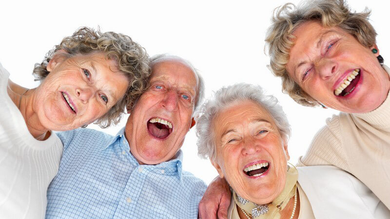 Gruppe alter Menschen lacht in Kamera, weißer Hintergrund