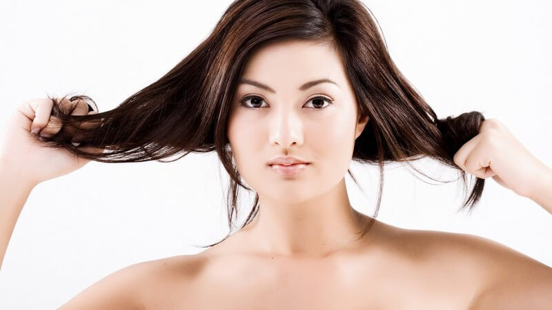 Asiatische junge Frau zieht an ihren Haaren, weißer Hintergrund