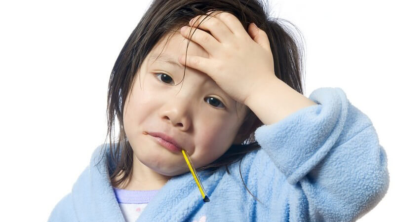 Kleines trauriges Mädchen hat Fieberthermometer im Mund, hält Hand vor Stirn
