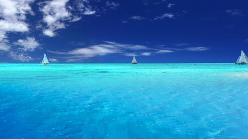 Hellblaues Meer mit 2 Segelbooten, blauer Himmel und weiße Wolken