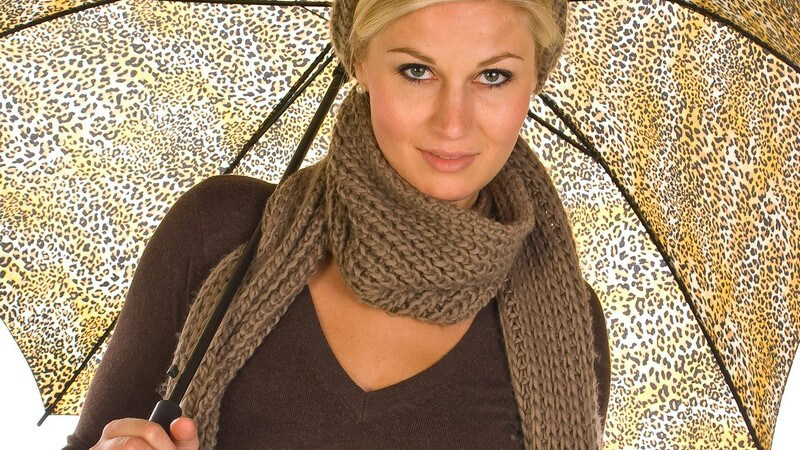 Junge Frau mit Schal und Mütze steht unter Regenschirm