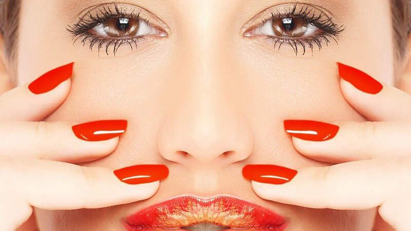 Gesicht und Finger einer jungen Frau, rote Fingernägel, rote Lippen