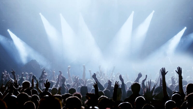 Menschenmenge wird von Scheinwerfern bestrahlt, Fans auf einem Konzert