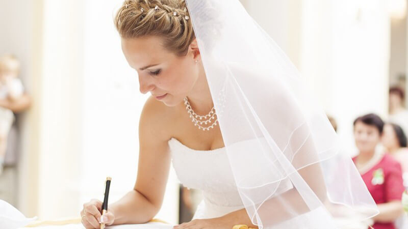 Hübsche Braut mit Schleier bei der Unterschrift im Standesamt