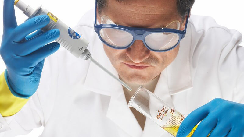 Laborarzt mit Schutzbrille füllt Probe in Reagenzglas