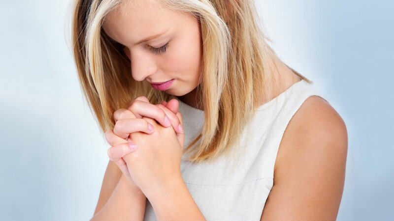 Seitenansicht junge Frau beim Beten, hellblauer Hintergrund