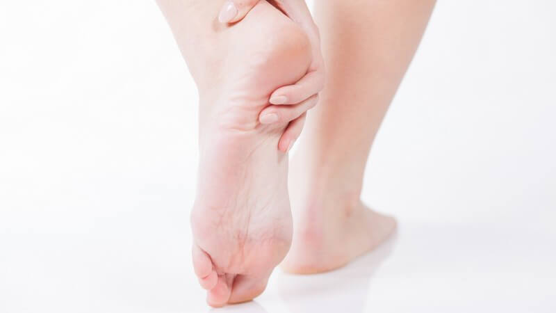 Frau mit Fersenschmerzen fasst sich an den linken Fuß