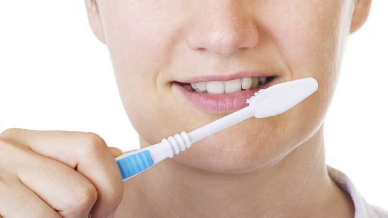 Unterer Teil des Gesichts einer Frau, die im Begriff ist, sich mit der rechten Hand die Zähne mit Zahnbürste zu putzen