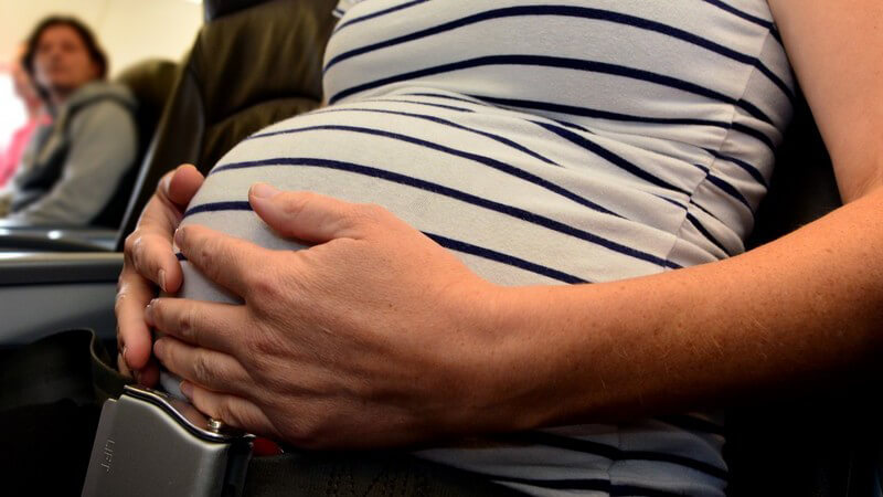 Bauch einer schwangeren Frau, sie hat die Hände darauf gelegt und sitzt im Flugzeug