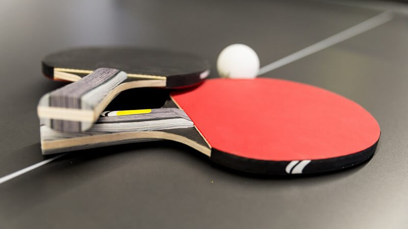 Schwarzer und roter Tischtennisschläger neben Ball auf Tischtennisplatte