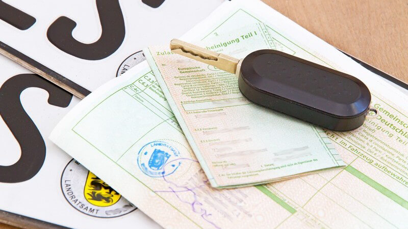 Autoschlüssel, Fahrzeugschein und Fahrzeugbrief liegen auf KFZ-Kennzeichen