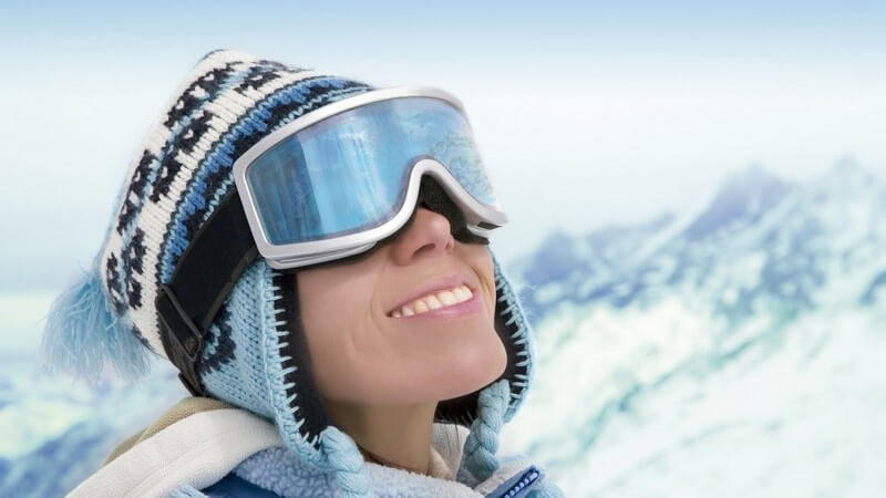 Junge Frau mit Strickmütze und Skibrille, dahinter Berg Panorama