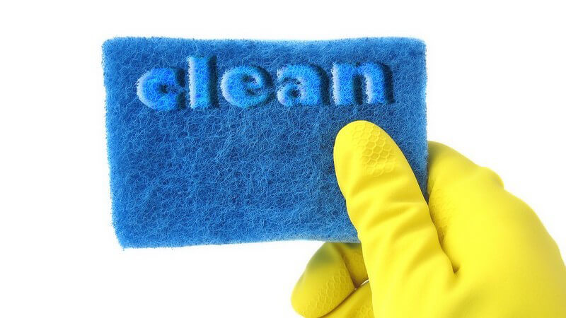 Hand in Spülhandschuh hält blauem Schwamm mit Aufschrift "Clean"