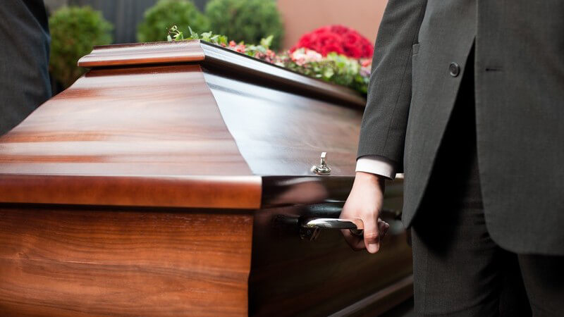 Beerdigung - Holzsarg wird von Männern im schwarzen Anzug getragen