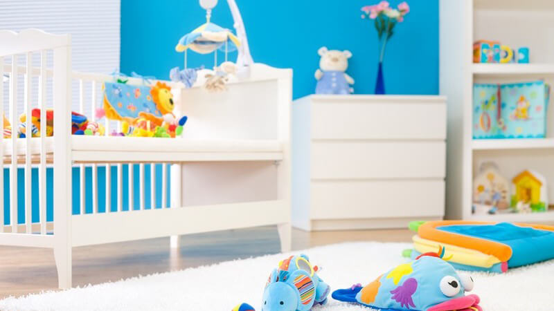 Ausschnitt Kinderzimmer mit blauer Wand, weißen Möbeln, buntem Spielzeug
