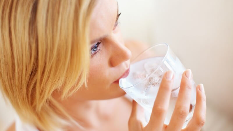 Junge Frau trinkt aus Glas mit Wasser