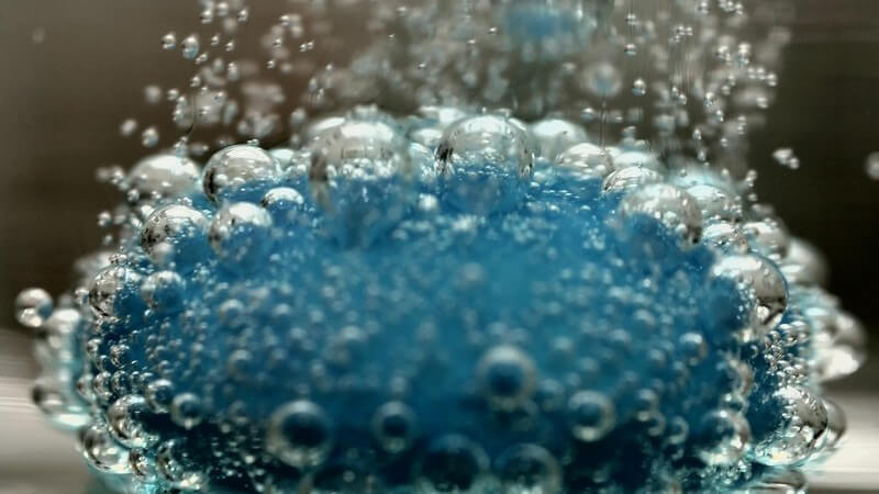 Blaue Brausetablette im Wasser, aus der viele Luftblasen aufsteigen