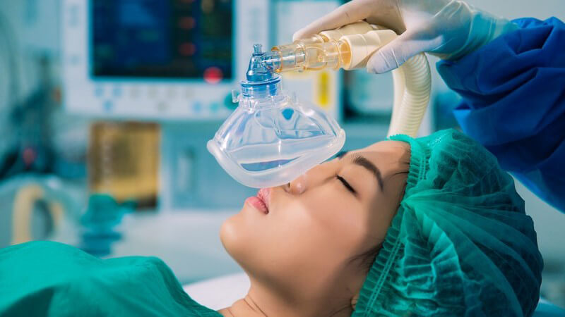 Asiatische Patientin bekommt im OP-Saal eine Maske zur Vollnarkose aufgesetzt