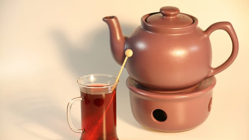 Teekanne mit Stövchen, daneben Glas mit Tee