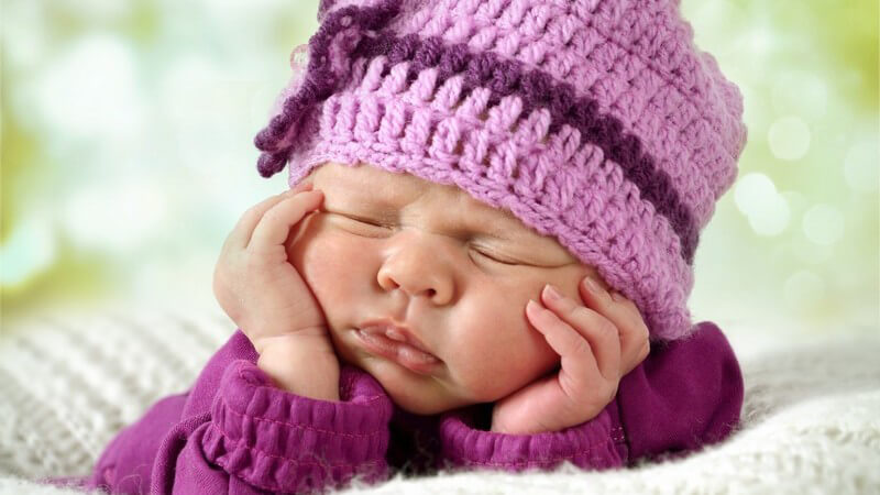 Babyfoto eines Neugeborenen mit lila Wollmütze