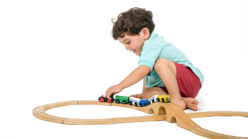 Kleiner Junge spielt mit Holzeisenbahn, weißer Hintergrund