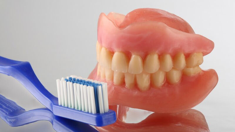 Gebiss mit gelblichen Zähnen neben blauer Zanbürste auf Spiegeluntergrund
