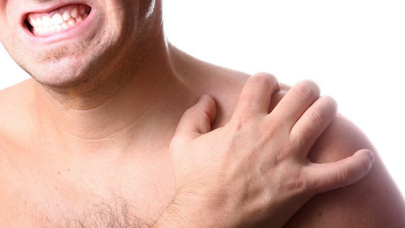 Mann hält mit schmerzverzerrter Hand linke Schulter