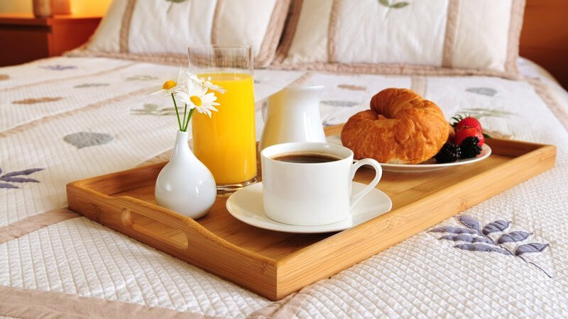 Frühstückstablett für Frühstück im Bett mit Kaffee, Orangensaft, Croissant und Früchten auf Ehebett