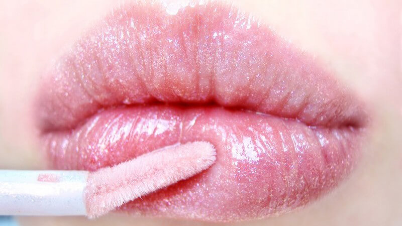 Nahaufnahme Lippen einer Frau mit rosa-schimmerndem Lipgloss und Applikator