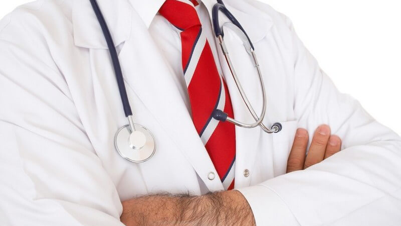 Brustpartie eines Arztes mit verschränkten Armen, rot-gestreifter Krawatte und Stetoskop um den Hals, weißer Hintergrund