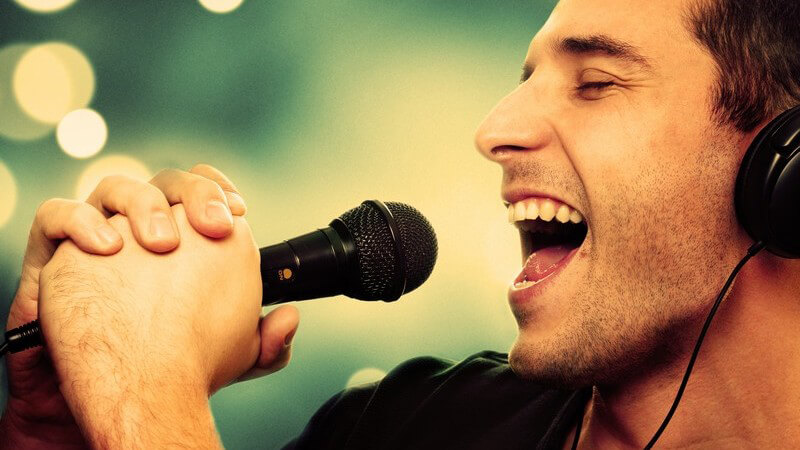 Sänger, junger Mann singt in ein Mikrofon und trägt Kopfhörer