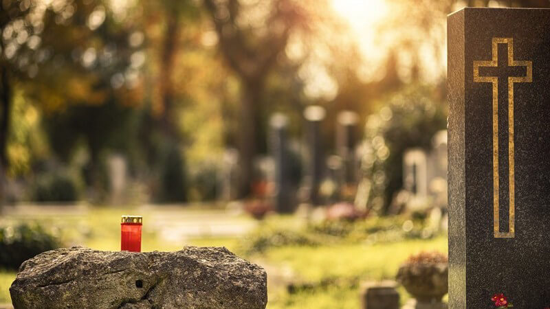 Friedhof bei Sonnenuntergang, Grablicht auf einem Stein neben einem Grabstein mit Kreuz drauf