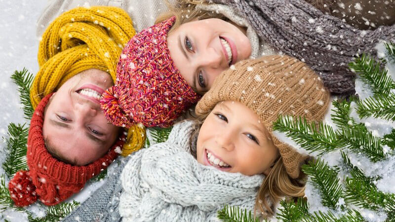 Vater, Mutter und Tochter liegen mit Wintermütze und Schal im Schnee