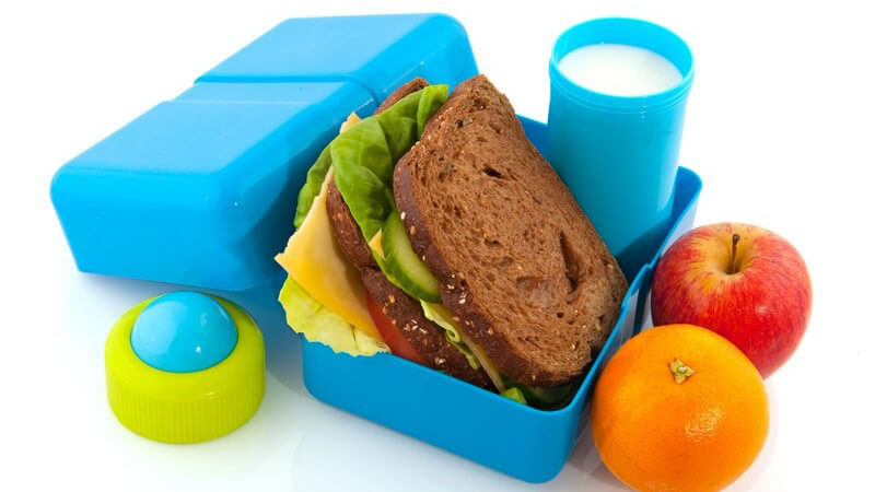 Lunchbox mit Brot, Obst und Milch auf weißem Hintergrund