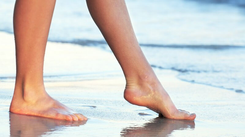 Frauenbeine am Wasser, Frau geht mit nackten Füße am Strand spazieren