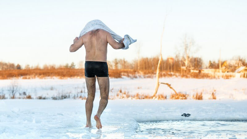 Mann läuft mit Handtuch über einen zugefrorenen See nach einem Bad im Eiswasser